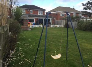 unlandscaped back garden with child's swing in the foreground and a row of large modern homes to the rear of the image